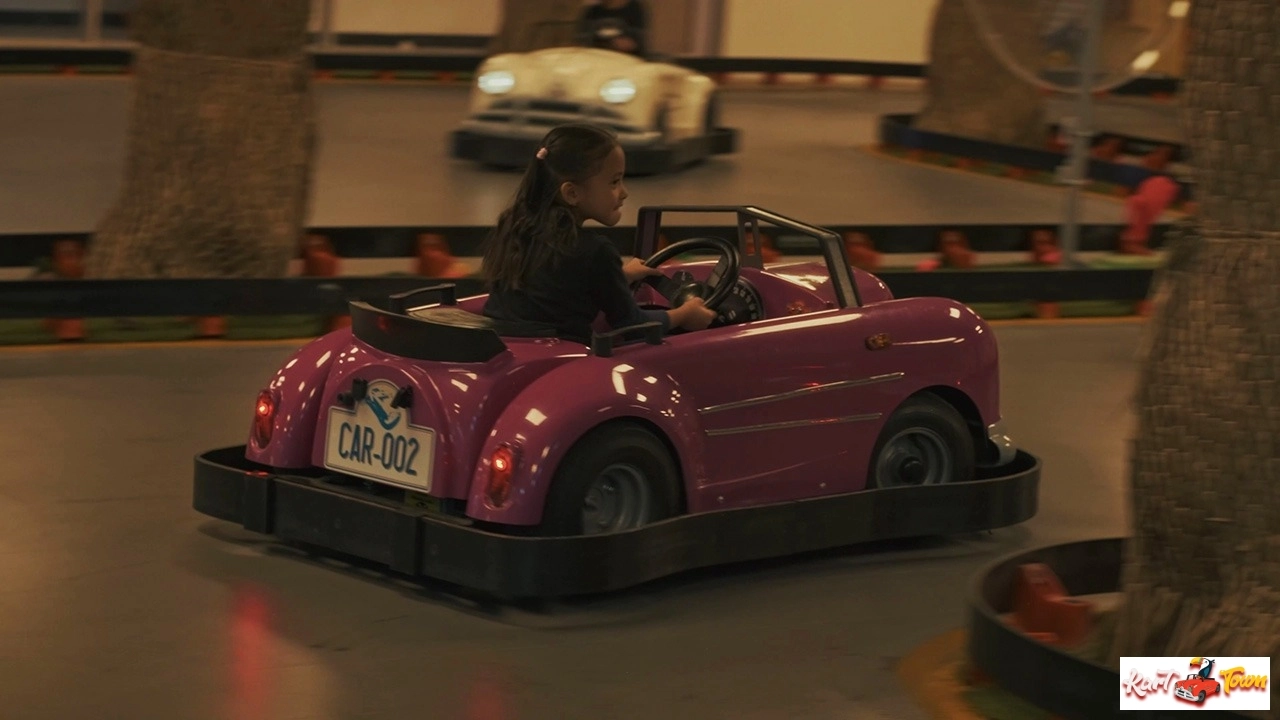 Person with a ponytail holding the steering wheel of a purple bumper car marked “CAR-002,” with another car in the background.