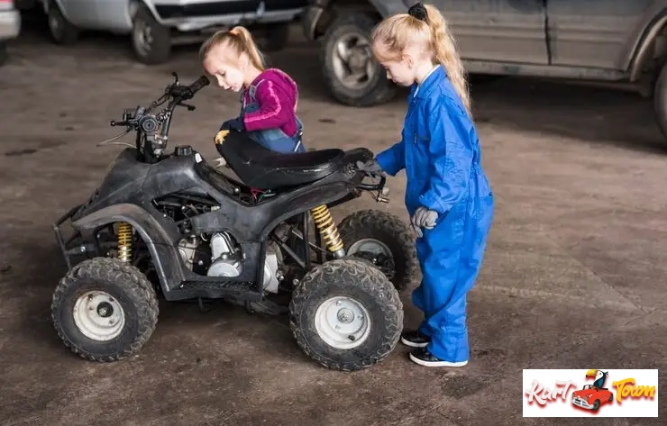 Two young girls examining a small ATV/quad bike in a garage setting.
