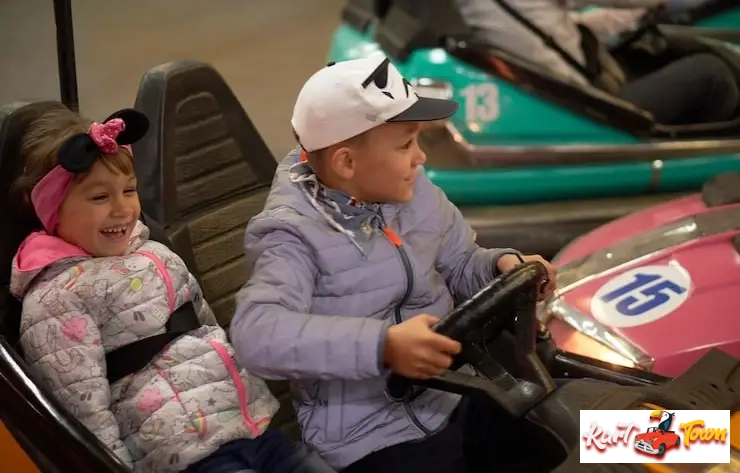 Boy steering a kiddie bumper car with a younger girl laughing next to him.