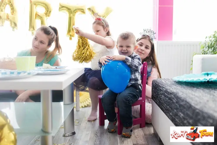 Four children celebrating a birthday in a bright room decorated with 'PARTY' balloons.