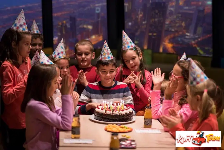 A group of children wearing party hats gathered around a table to celebrate a birthday.