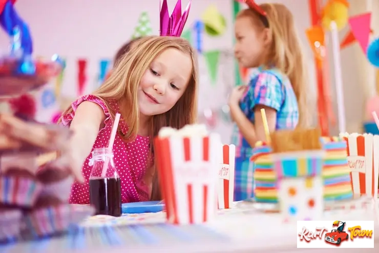 A close-up of a young girl, smiling as she reaches for a drink bottle.
