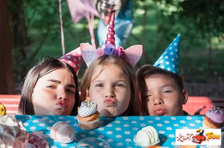 Three happy children wearing party hats and unicorn headbands, posing with cupcakes.
