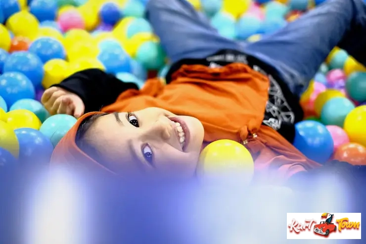 A smiling child lying on their back in a colorful indoor ball pit.