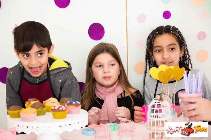 Three children participate in a cupcake decorating activity at a birthday party.