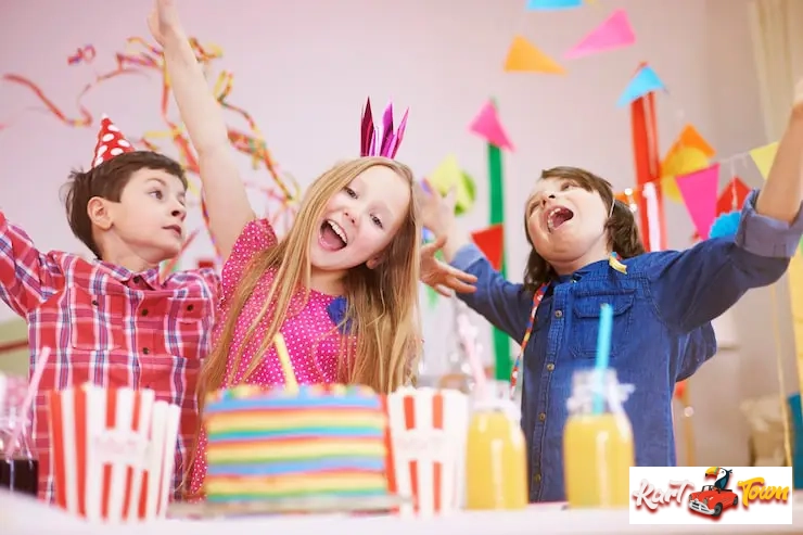 Three ecstatic children with their arms raised, standing behind a colorful birthday cake.