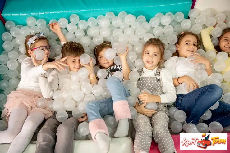 A group of cheerful children lying in a large indoor ball pit filled with clear.