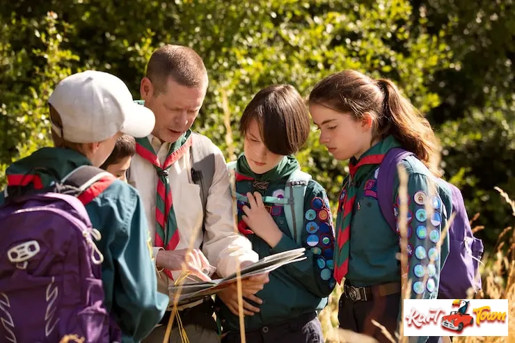 Scout leader and three young scouts in uniform studying a map in a sunny.
