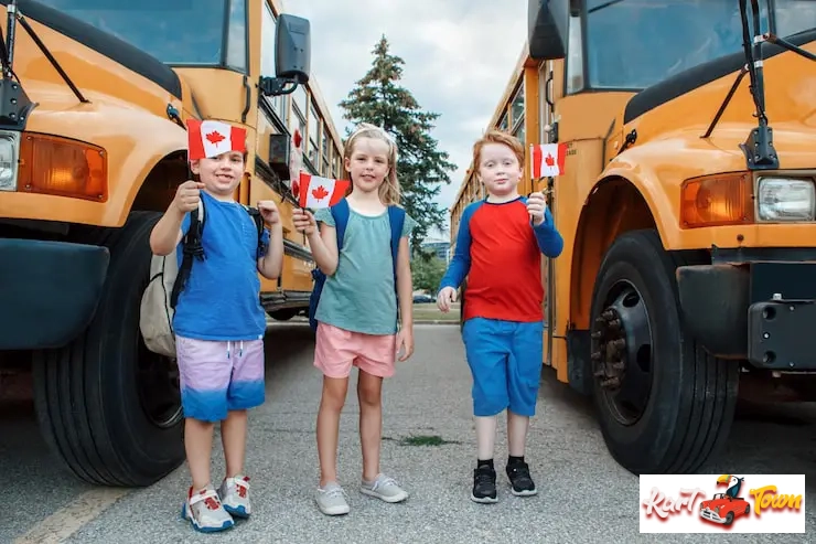 Three smiling elementary school children standing between two yellow school buses.