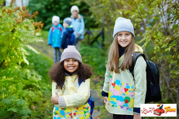 Two young girls in raincoats and hats smiling for the camera on a nature trail.