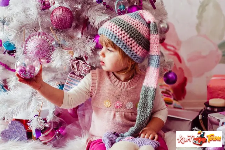 Toddler wearing a long, striped knitted hat, touching a sparkly ornament.