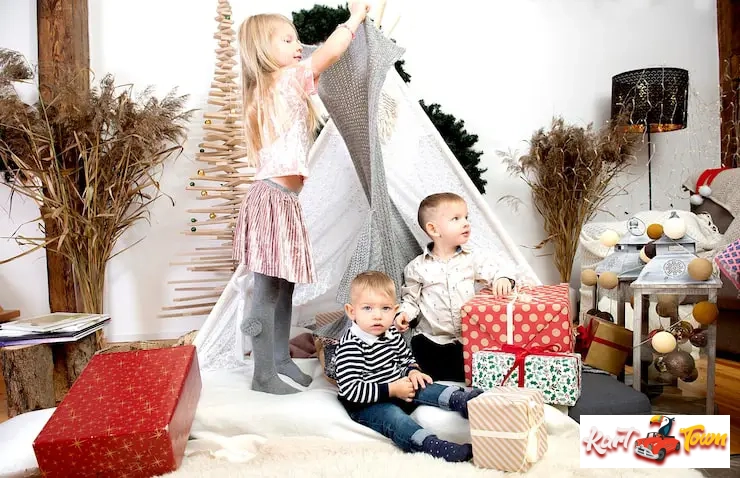 Three young children playing near a teepee.
