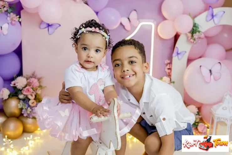 Siblings posing at a first birthday party with purple, pink, and butterfly decor.