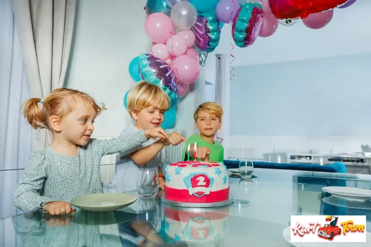 Three children gather excitedly around a birthday cake at an indoor party.