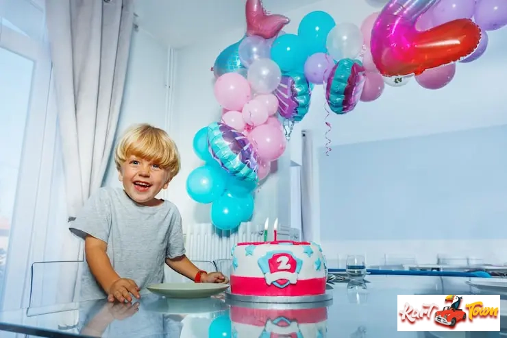Happy blonde boy smiles widely next to a birthday cake decorated with "2".