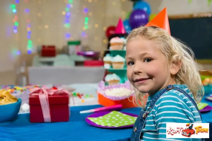 A blonde child in a party hat and overalls smiles at an indoor birthday party venue in Toronto.
