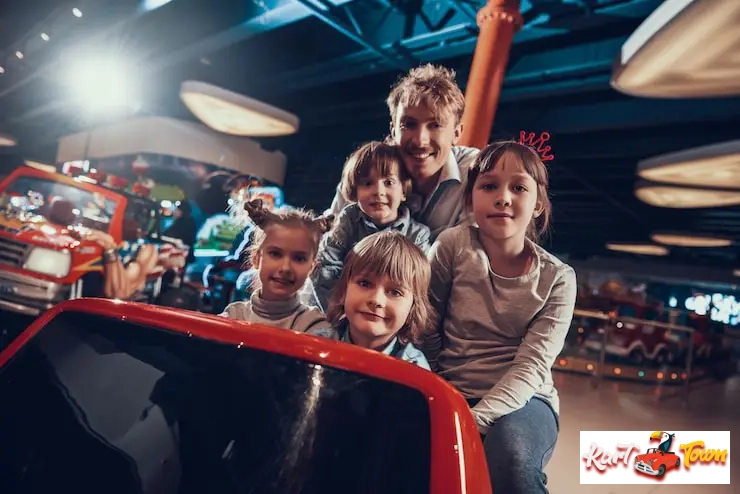 A group of children and an adult posing together on a ride at an indoor entertainment facility.