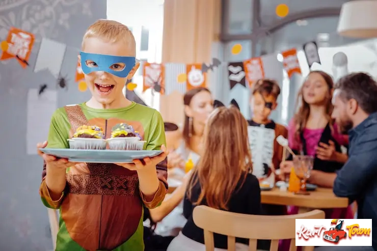 Boy in superhero costume holding cupcakes at a party