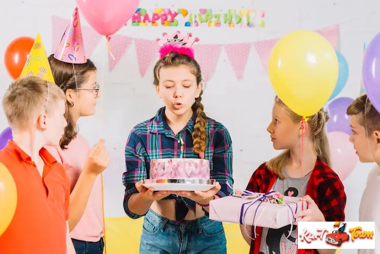 Girl blowing out birthday candles surrounded by friends and balloons.