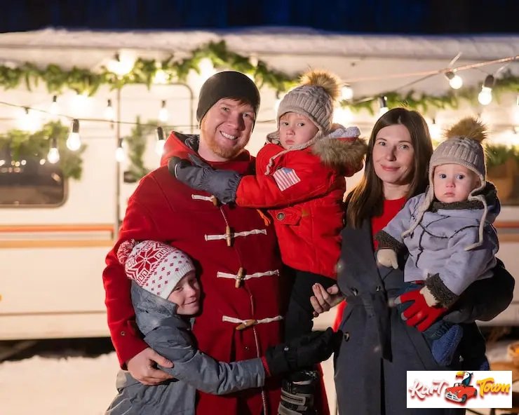 Happy family posing by a decorated holiday trailer.
