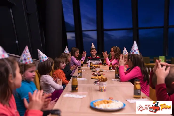 A group of kids in party hats sitting around a long table clapping during a celebration.