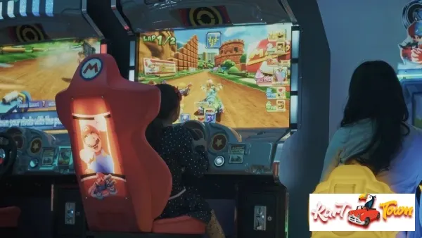 Two people sit at Mario Kart arcade racing machines with steering wheels, colorful game screens, and red and yellow seats.