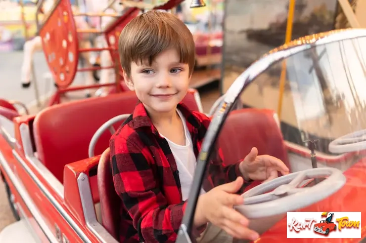 A smiling young boy "driving" a red toy car at a fair.