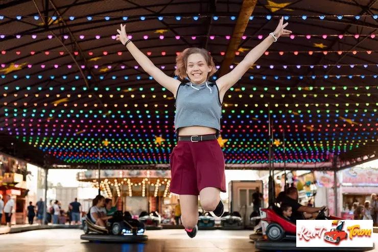 A happy girl jumping in front of an indoor bumper car rink.
