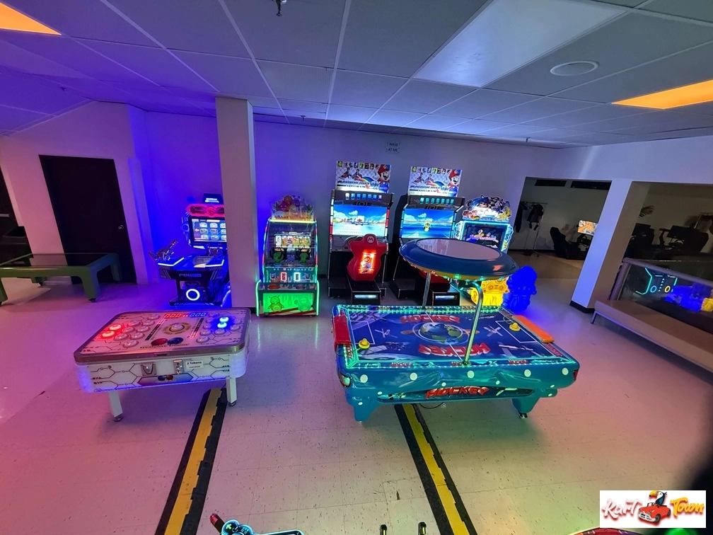 Colorfully lit arcade machines line a wall behind an air hockey table and a two-player tabletop game.