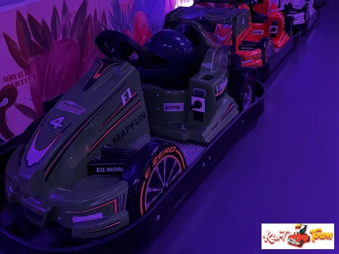 A row of race car-shaped seats under purple lighting, with a green number 4 car and black helmet in front.