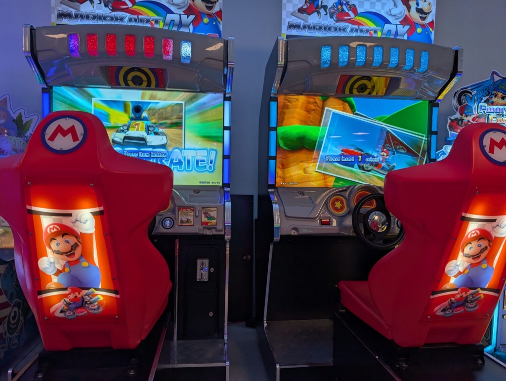 Kids racing side by side on Mario Kart arcade machines in the bright arcade at Kart Town