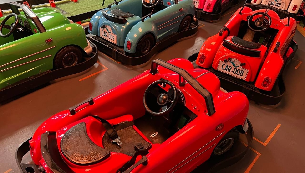 Fleet of pastel classic ride-on cars in green, blue, red, pink and white parked on grid