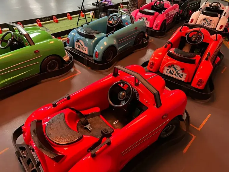 Fleet of pastel classic ride-on cars in green, blue, red, pink and white parked on grid