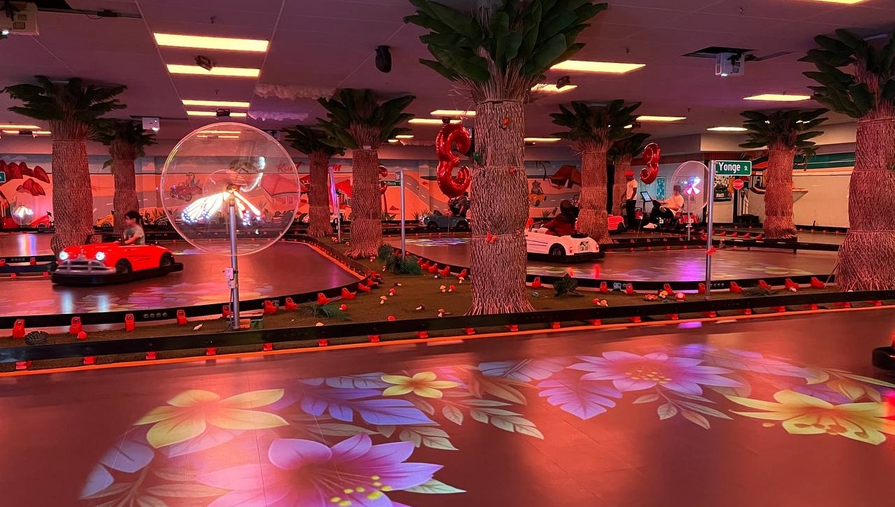 Kart Town indoor track lit in neon red with karts racing, palm trees and floral projections