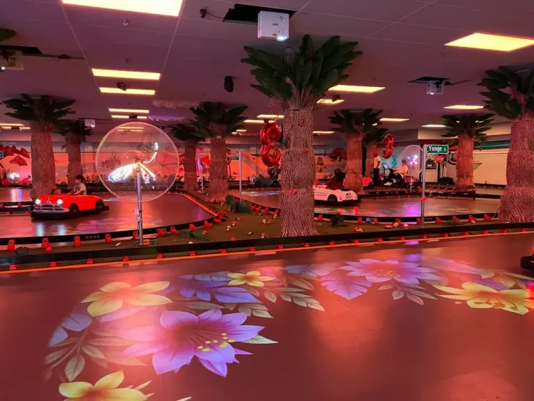 Kart Town indoor track lit in neon red with karts racing, palm trees and floral projections