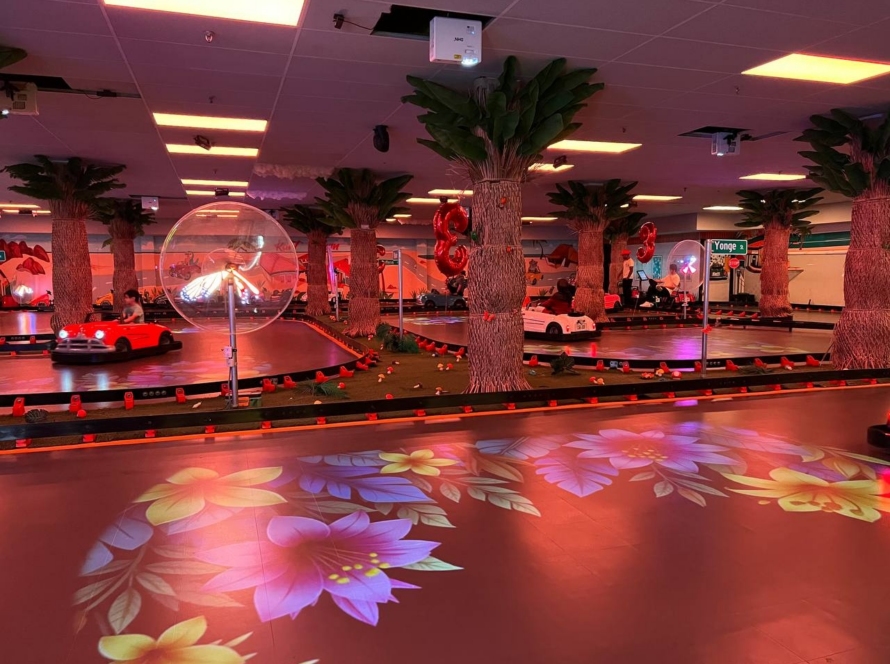 Kart Town indoor track lit in neon red with karts racing, palm trees and floral projections
