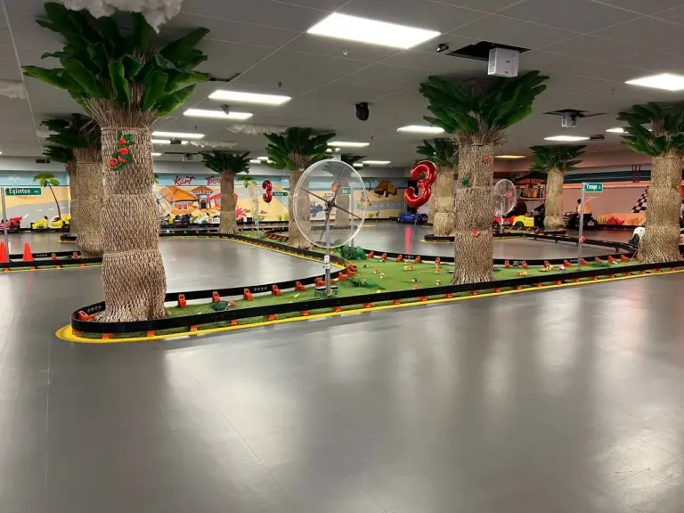 Empty indoor go-kart track with palm trees, murals and 3rd anniversary balloon decorations