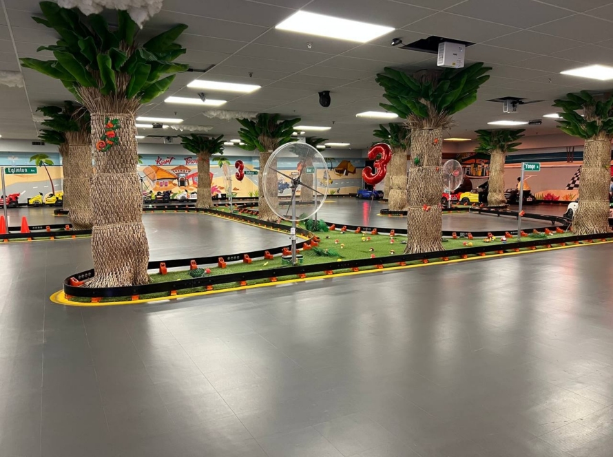 Empty indoor go-kart track with palm trees, murals and 3rd anniversary balloon decorations