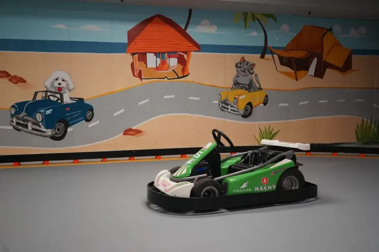 Green convertible go-kart on the track beside the painted desert and cactus mural