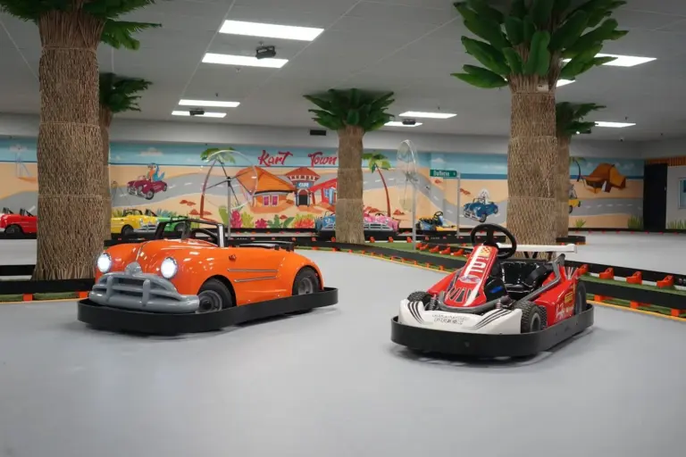 Orange and red go-karts parked on the indoor track among the palm trees