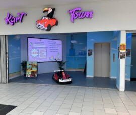 The bright Kart Town entrance — our toucan mascot welcomes families to a day of racing and play. Kart Town storefront entrance with toucan-and-red-car sign, party sign board and welcome kart