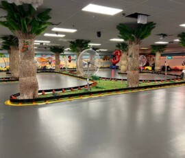 A quiet moment on our themed indoor track — palm trees, mural backdrop and racing lanes ready to go. Empty indoor go-kart track with palm trees, murals and 3rd anniversary balloon decorations