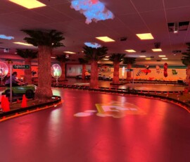 Sweeping curves under warm red lighting — the perfect setting for a birthday race lap. Sweeping curve of the Kart Town track lit in red with palm trees and a green kart passing