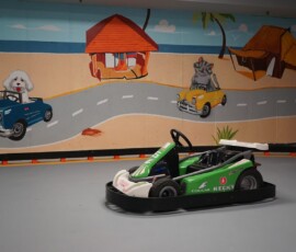 Race past our hand-painted desert mural down the straightaway. Green convertible go-kart on the track beside the painted desert and cactus mural