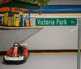 Pull up to our themed pit-stop gas station along the track. Go-kart beside the themed gas station prop on the indoor track
